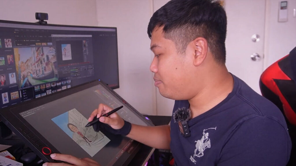 ช่างเหินกำลังวาดภาพการ์ตูนดิจิตอลด้วยเมาส์ปากกาบนหน้าจอวาดภาพ พร้อมหน้าจอคอมแสดงผลงานศิลปะดิจิตอลหลากหลายแบบ