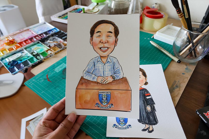 วาดรูปเป็นของขวัญ เหมาะกับโอกาสไหนบ้าง? ภาพวาดการ์ตูนล้อเลียนผู้ชายยืนหลังโพเดียมบนกระดาษ พร้อมอุปกรณ์วาดรูปบนโต๊ะ