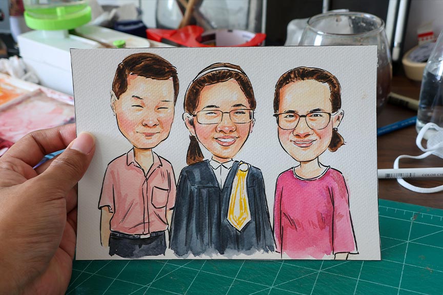 ภาพการ์ตูนล้อเลียนสามคน มีบัณฑิตสวมชุดครุยยืนกับครอบครัวบนกระดาษวาดรูป